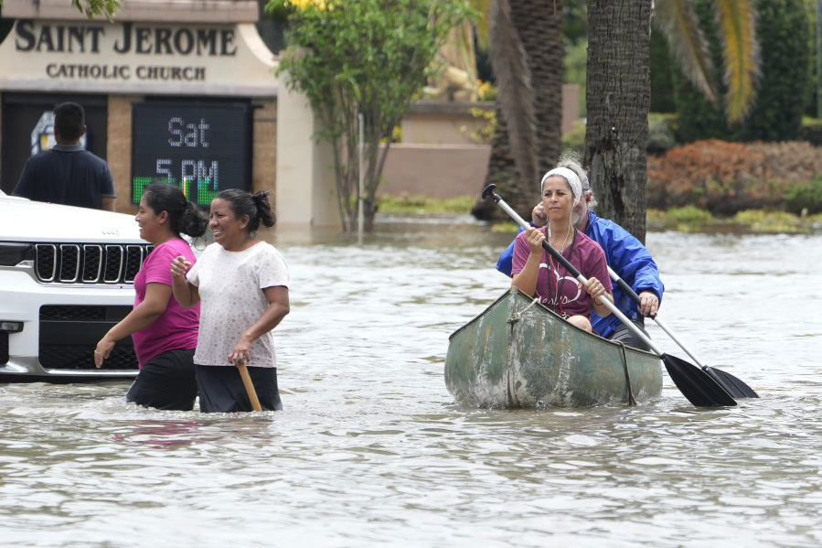 Residents paddle and walk along a flooded road Thursday, April 13, 2023, in Fort Lauderdale, Fla. Over two feet of rain fell causing widespread flooding, closing the Fort Lauderdale airport and turning thoroughfares into rivers.