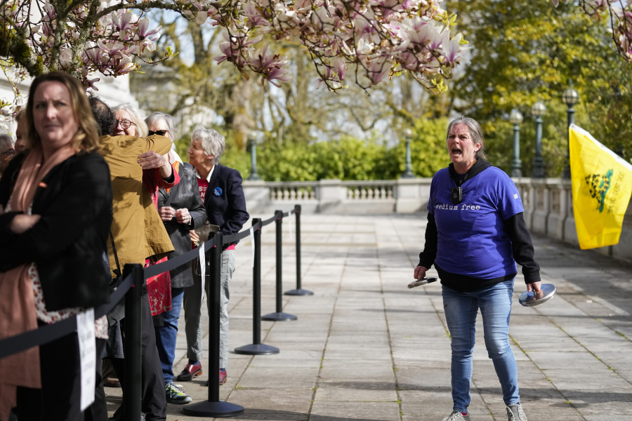 Sara Jones, right, with "We the People Against Communism," yells at guests lining up to enter the Capitol while she protests ahead of the signing of firearms regulation bills by Washington Gov. Jay Inslee, Tuesday, April 25, 2023, in Olympia, Wash.