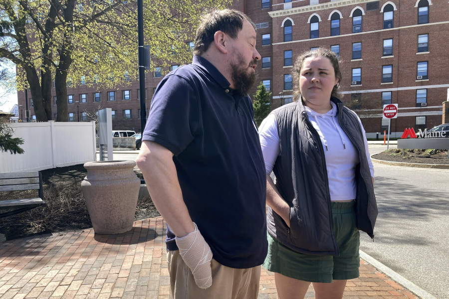 Sean Halsey, left, who was injured along with his children (not shown) in a shooting in Maine last week, speaks at a news conference outside Maine Medical Center in Portland, Maine, Friday, April 28, 2023, as family friend Haley Murphy, right, listens on. Halsey said he and his children are recovering from their injuries and grateful for the support they've received from the community. A 34-year-old man confessed last week to four killings at a home in Bowdoin and injuring the three people while shooting at vehicles on Interstate 295 in Yarmouth, police have said.