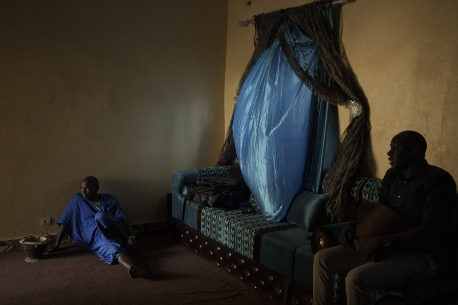Adama Barra, right, and a relative, sit in his living room in Selibaby, Mauritania, Wednesday, Dec. 8, 2021. Barra, a local teacher, knew many of the young men who went missing after boarding a boat in Nouadhibou hoping to reach Spain's Canary Islands.