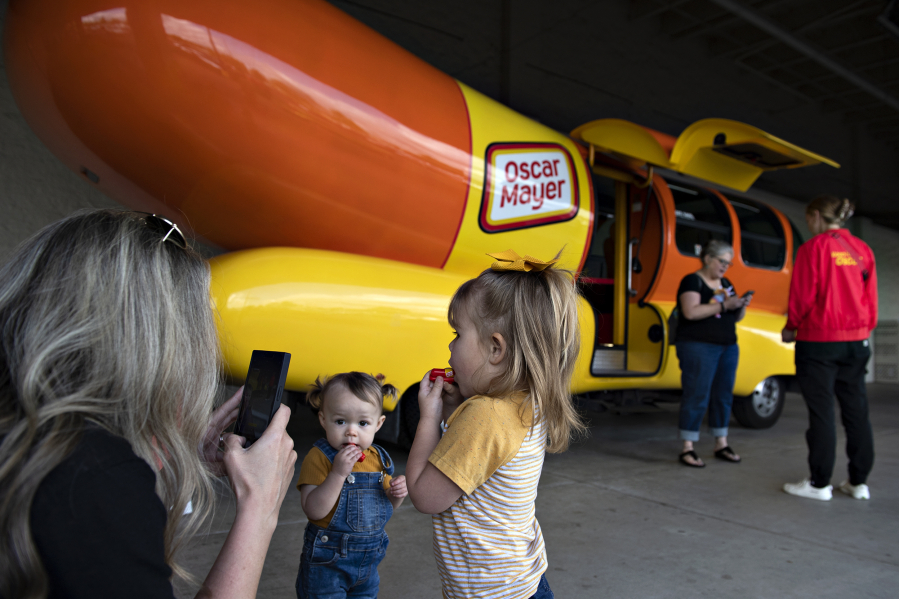 Melissa Stroud of Ridgefield, from left, pauses to snap a photo of her nieces, Mabel Gaussoin, 1, and her sister, Olivia, 3, as they test out their hot dog-shaped "weenie whistles" after visiting the Wienermobile at the Cascade Park Safeway on Tuesday afternoon.