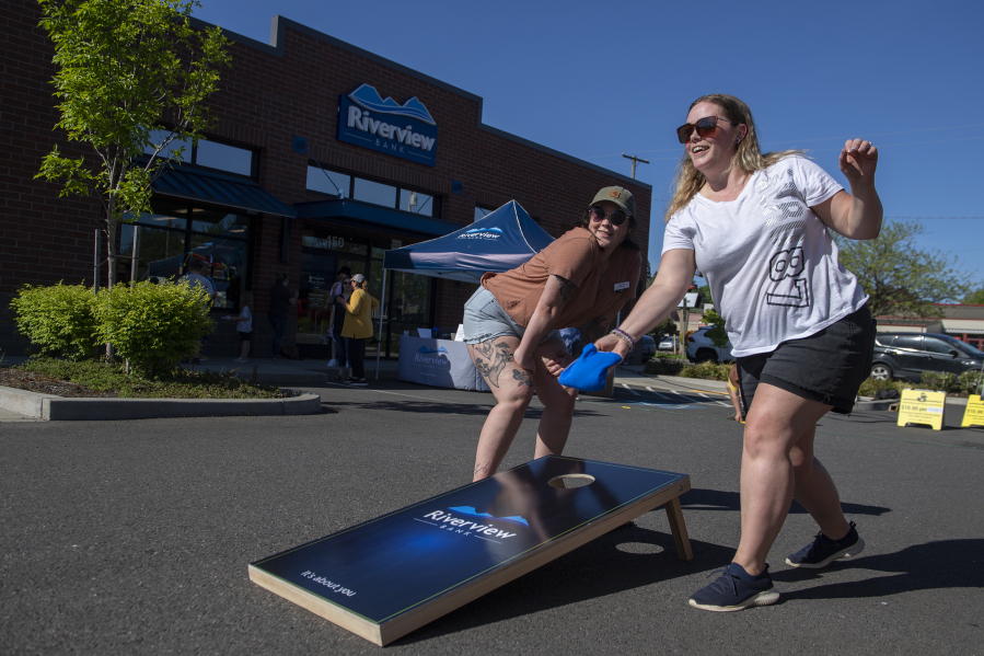 Riverview Bank employees Faith Salyers, left, and Molly Helige test their luck during a game of cornhole while celebrating the 100th anniversary of the bank in Camas on Friday afternoon.