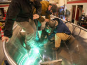 Clark College student Hallie Tibbit, right, welds a bar to the bottom of a metal boat as River Fortier, center, watches during an Advanced TIG (tungsten inert gas) welding class at Clark College. The boat, the students' final project, will be put to the test at Lacamas Lake in less than three weeks, a rite of passage for those graduating from the program, a symbolic send-off to their next adventure.