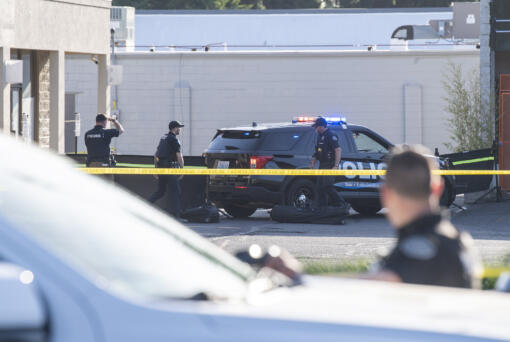 Vancouver Police officers stand outside a barricade that hides a body on Tuesday, May 30, 2023, at the site of a fatal shooting in the Heights Shopping Center parking lot.