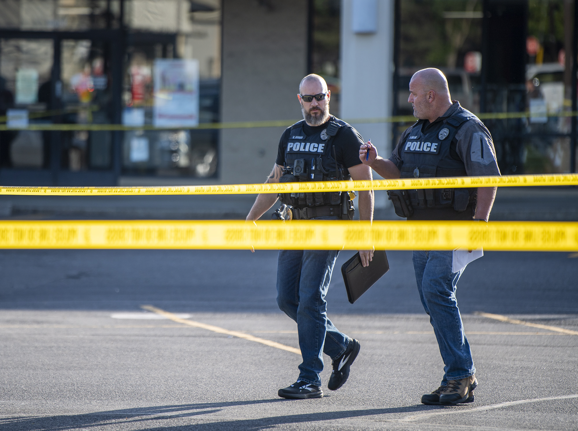 Police officers walk behind crime scene tape Tuesday, May 30, 2023, at the site of a fatal shooting in the Heights Shopping Center parking lot.