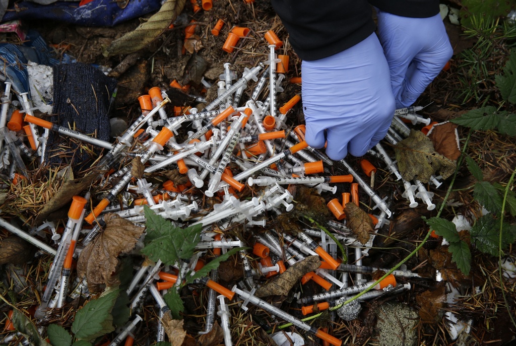 FILE - A volunteer cleans up needles used for drug injection that were found at a homeless encampment in Everett, Wash., Nov. 8, 2017. (AP Photo/Ted S.