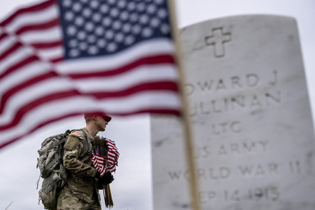 A member of the 3rd U.S. Infantry Regiment, also known as The Old Guard, places flags in front of each headstone for "Flags-In" at Arlington National Cemetery in Arlington, Thursday, May 25, 2023, to honor the Nation's fallen military heroes ahead of Memorial Day.