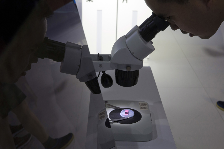 FILE - A visitor to the 21st China Beijing International High-tech Expo looks at a computer chip through the microscope displayed by the state-controlled Tsinghua Unigroup project which has emerged as a national champion for Beijing's semiconductor ambitions in Beijing, on May 17, 2018. Britain's government unveiled its long-awaited semiconductor strategy Friday, May 19, 2023 catching up with similar efforts by Western allies seeking to reduce reliance on Asian production of the computer chips that are essential to modern life.
