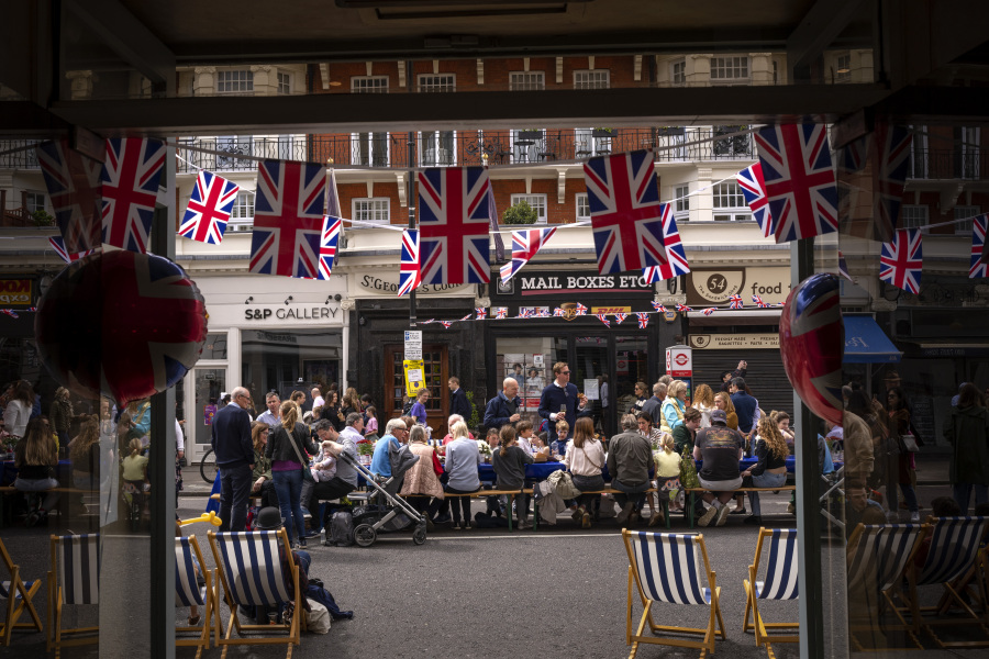 People eat their lunch sitting at big tables in the street as part of the Big Lunch celebration in London, Sunday, May 7, 2023. The Big Lunch is part of the weekend of celebrations for the Coronation of King Charles III.