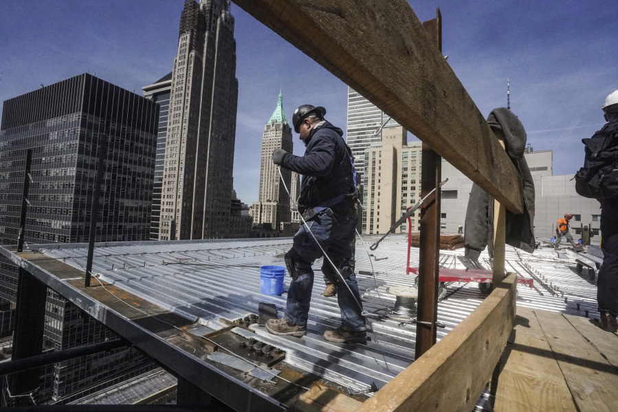 File - Construction workers install roofing on a high rise in Manhattan's financial district on Tuesday, April 11, 2023, in New York. On Friday, the U.S. government issues the April jobs report.