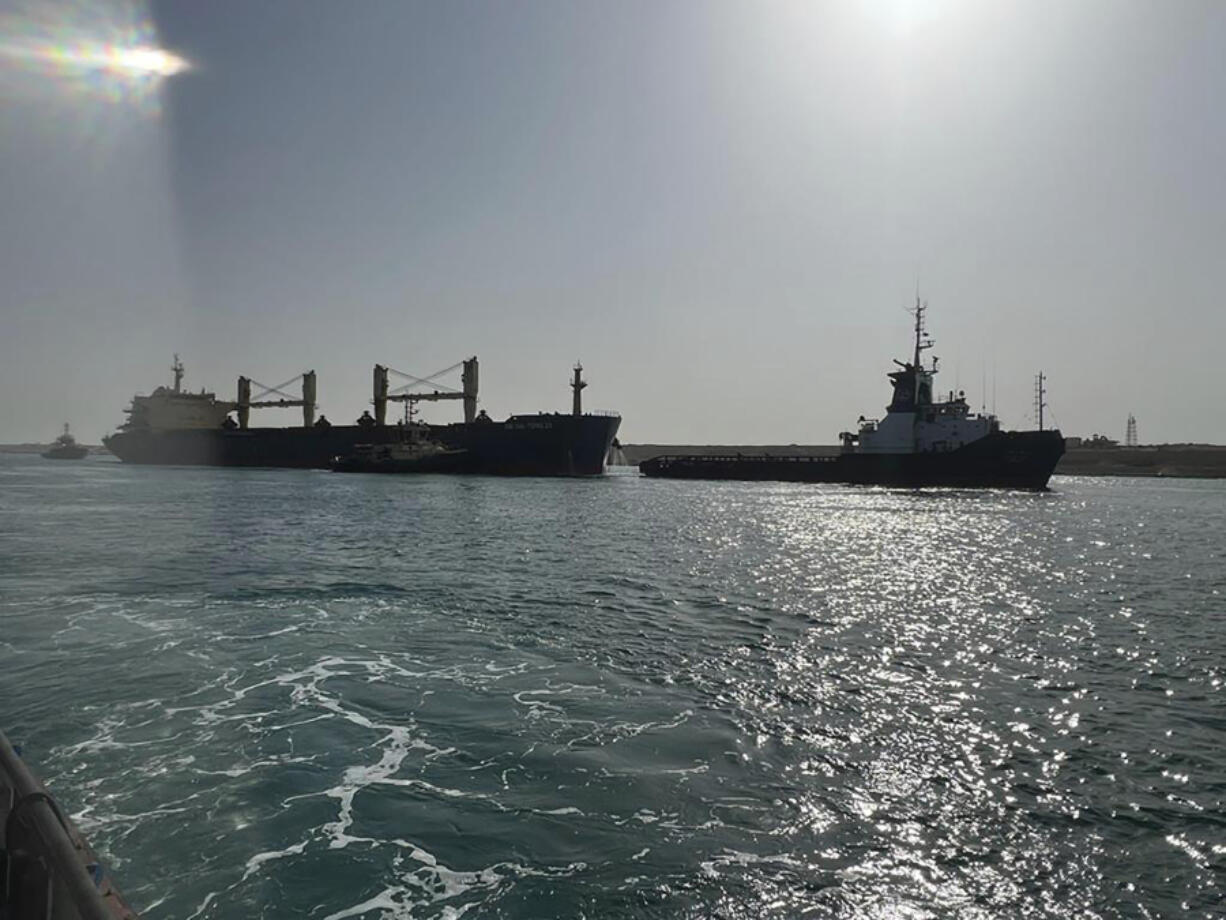 In this photo provided by The Suez Canal Authority in Egypt, the bulk carrier ship Xin Hai Tong 23, left, is towed after it ran aground at the southern mouth of the Suez Canal Thursday, May 25, 2023. The ship was being towed to another area by three tug boats after an "emergency malfunction," the authority said, that caused it to stop sailing, a rescue team of tugboats refloated it soon after.