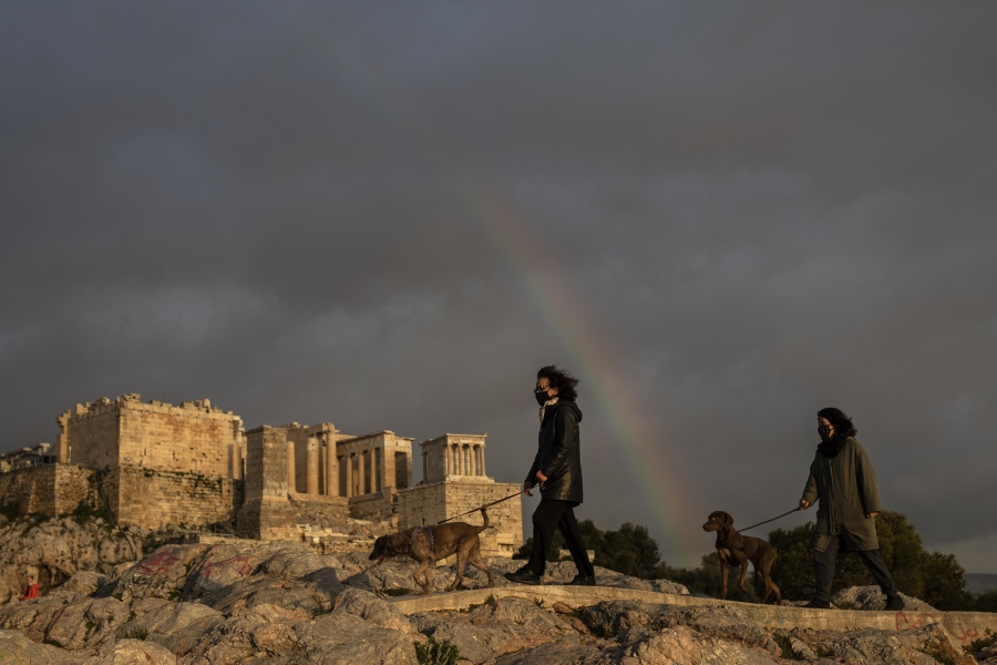 Women wearing face masks walk with their dogs March 31, 2021, at the Areopagus hill, in front of the ancient Acropolis hill, as a rainbow is seen in the Athenian sky.