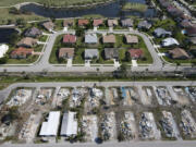 In this photo taken with a drone, the remains of homes demolished after sustaining heavy damage in Hurricane Ian are seen in Tropicana Sands mobile home park, bottom, in Fort Myers, Fla., Wednesday, May 10, 2023. More than seven months after the storm, crews continue  removing debris after demolishing all but a handful of the hundreds of manufactured homes in the community marketed to active adults ages 55 and up. The state estimated the total insured loss from Ian in Florida was almost $14 billion, with more than 143,000 claims still open without payment or claims paid but not fully settled as of March 9.