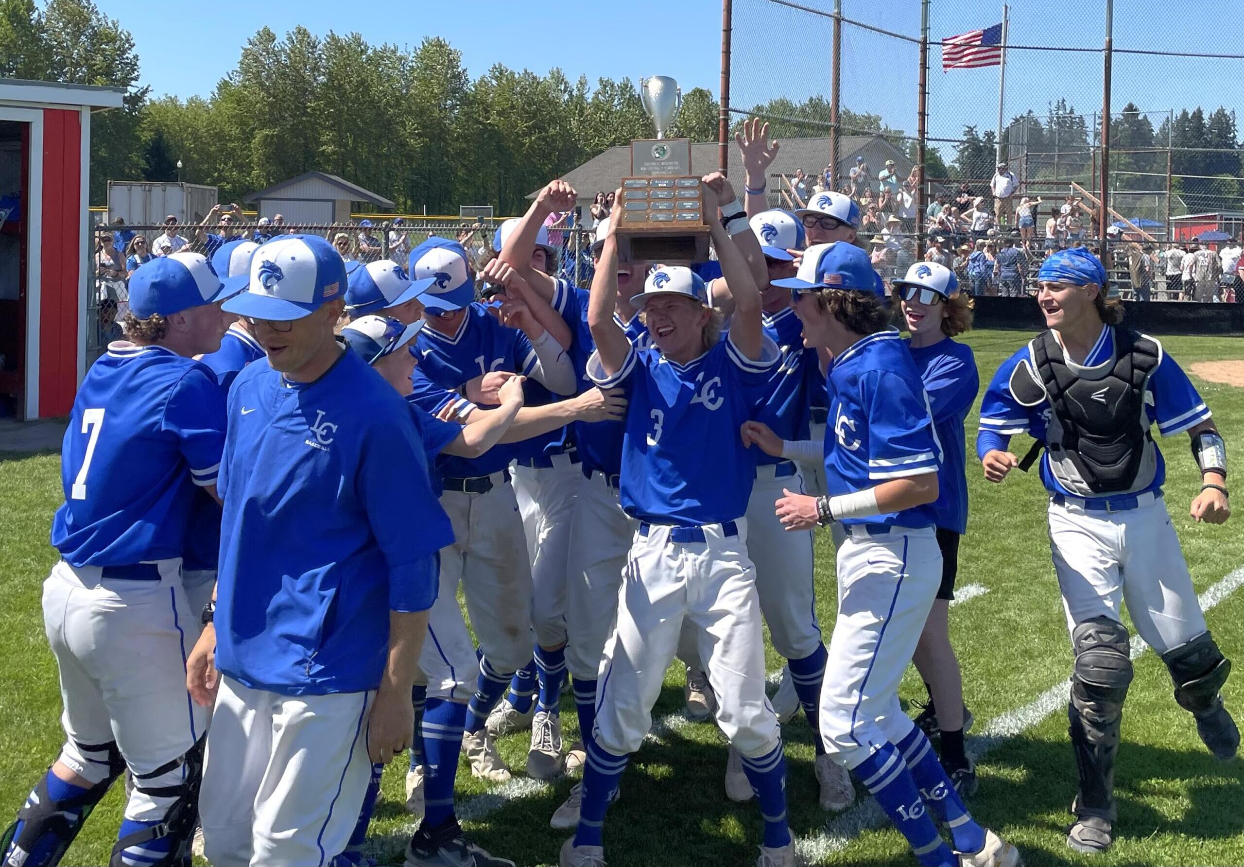 La Center’s Garrett Maunu (3) holds the 1A district baseball championship trophy as the Wildcats celebrate their third straight title with a 9-0 win over Montesano on Saturday, May 13, 2023, at Castle Rock High School.