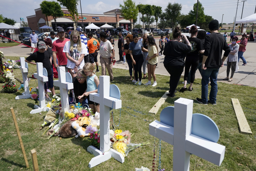 Jessica Himes, kneeling in front of cross, holds her daughter Harper, blue shirt, as her son Hudson, left in black shirt, her husband Scott, left rear in red shirt, and daughter Blakely Brooks, center left in white shirt, all from Allen, Texas, look on at a makeshift memorial by the mall where several people were killed in Saturday's mass shooting, Monday, May 8, 2023, in Allen, Texas.