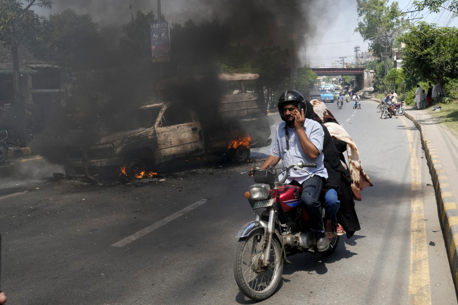 A motorcyclist drives past a burning vehicle set on fire by angry supporters of Pakistan's former Prime Minister Imran Khan, in Lahore, Pakistan, Thursday, May 11, 2023. With Khan in custody, Pakistani authorities on Thursday cracked down on his supporters, arresting hundreds in overnight raids and sending troops across the country to rein in the wave of violence that followed his arrest earlier this week. (AP Photo/K.M.