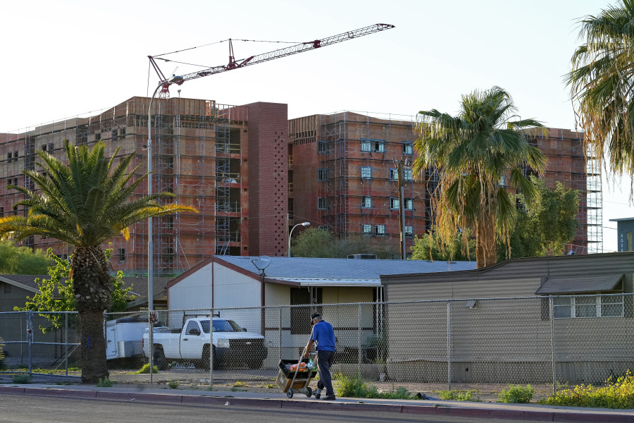 A man selling fruit walks past the fenced-off Periwinkle Mobile Home Park, Thursday, April 11, 2023, in Phoenix as new student housing is constructed in the background. Residents of the park are facing an eviction deadline of May 28 due to a private university's plan to redevelop the land for student housing.