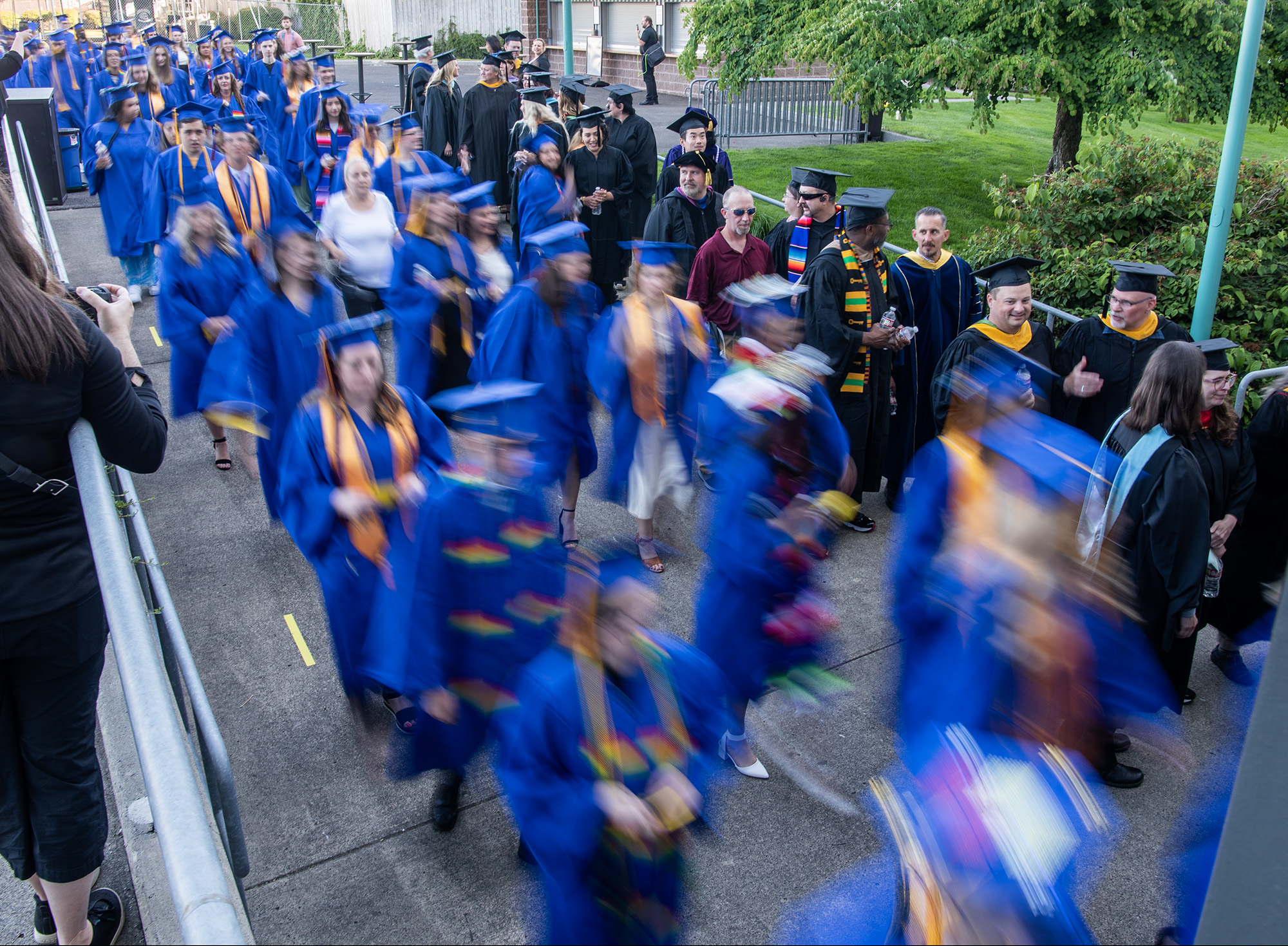 Graduates, in blue at left, and faculty, in black at right, walk into the RV Inn Style Resorts Amphitheater on Thursday, June 15, 2023, during the Clark College Commencement Ceremony.