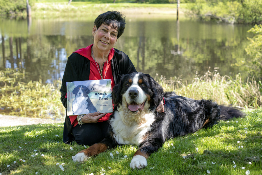 Michelle LeFevre and her Bernese mountain dog Kona sit in the shade in front of Kona???s Pond outside their home Wednesday, May 10, 2023, in Camano, Washington. LeFevre, a retired teacher, wrote the children???s book ???On Kona???s Pond??? which centers on her pup and the other creatures that call the pond home. LeFevre???s sister, Susan Cousineau McGough, illustrated the book with watercolor renditions of Kona and the pond.