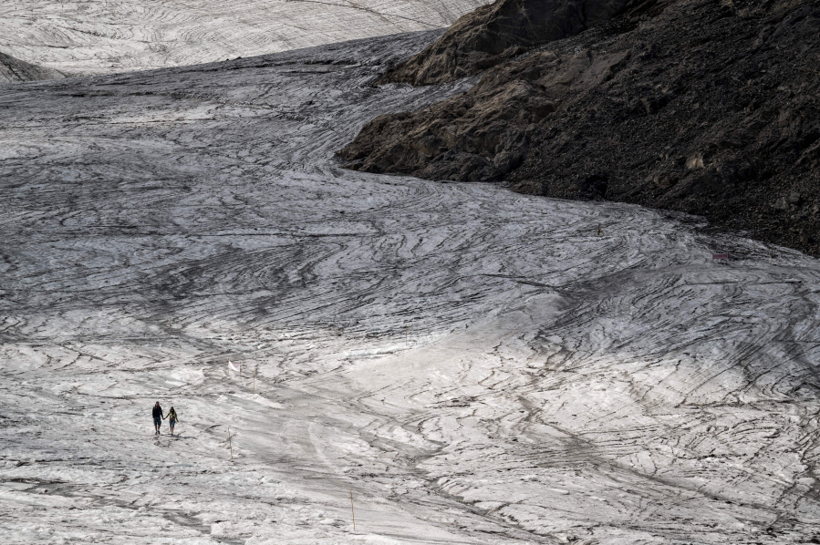A couple hold their hands while walking on the melting Tsanfleuron Glacier above Les Diablerets on Aug. 6, 2022. Following several heatwaves blamed by scientists on climate change, Switzerland is seeing its alpine glaciers melting at an increasingly rapid rate.