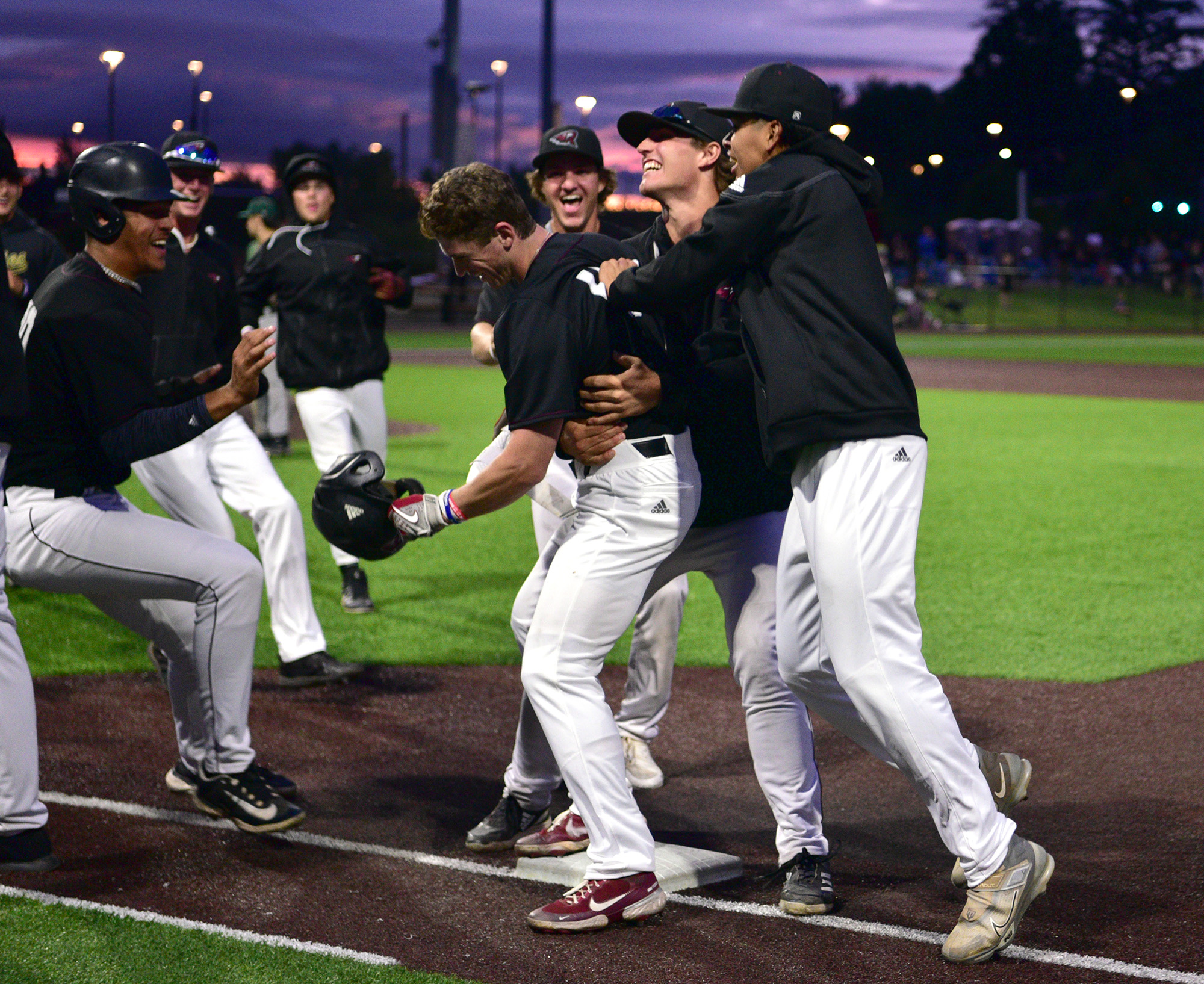 Raptors player Jackson Nicklaus, center, is mobbed by teammates Friday, June 16, 2023, after his walk-off two RBI single helped the  Raptors win 7-6 against Cowlitz at the Ridgefield Outdoor Recreation Complex.