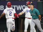 Seattle Mariners starting pitcher Bryan Woo, right, backs up the plate as Texas Rangers' Marcus Semien (2) celebrates with Nathaniel Lowe, center, after scoring on a Corey Seager single in the first inning of a baseball game, Saturday, June 3, 2023, in Arlington, Texas.