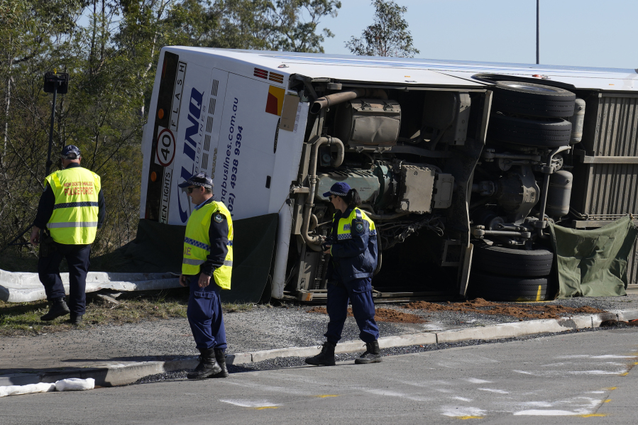 Police inspect a bus in its side near the town of Greta following a crash in the Hunter Valley, north of Sydney, Australia, Monday, June 12, 2023. The bus carrying wedding guests rolled over on a foggy night in Australia's wine country, killing and injuring multiple people, police said.