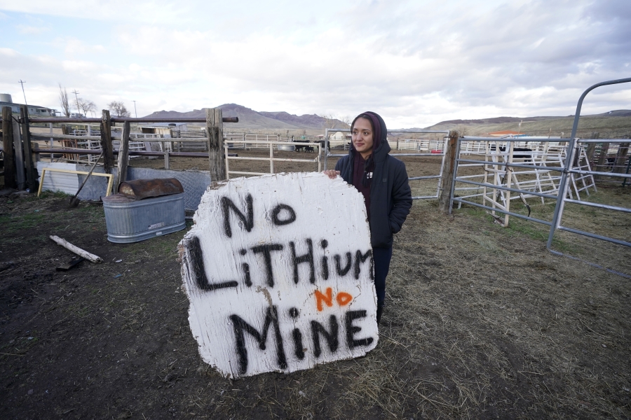 Daranda Hinkey, a Fort McDermitt Paiute and Shoshone tribe member, holds a large hand-painted sign that says "No Lithium No mine" at her home, on April 24, 2023, on the Fort McDermitt Indian Reservation, near McDermitt, Nev. The Biden administration says the project will help mitigate climate change by speeding the shift from fossil fuels. But Hinkey and other opponents say it is not worth the costs to the local environment and people.