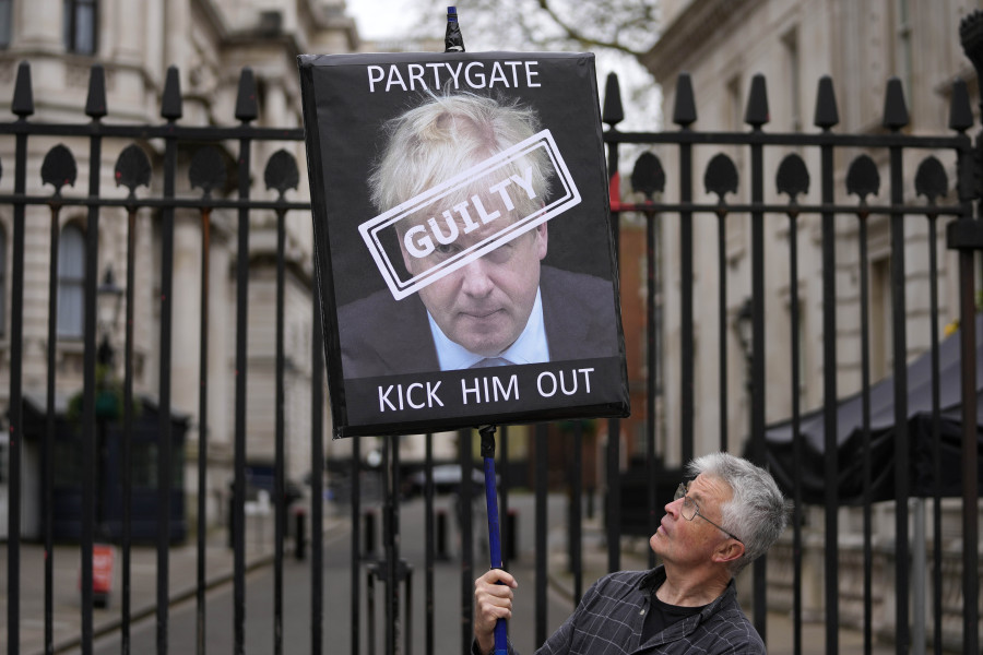 FILE - A protester holds a sign showing British Prime Minister Boris Johnson as he stands in front of the entrance to Downing Street in London, Wednesday, April 13, 2022. Former Prime Minister Boris Johnson deliberately misled Parliament about the lockdown-flouting parties that undermined his credibility and contributed to his downfall, a committee of lawmakers said Thursday, June 15, 2023 after a year-long investigation.