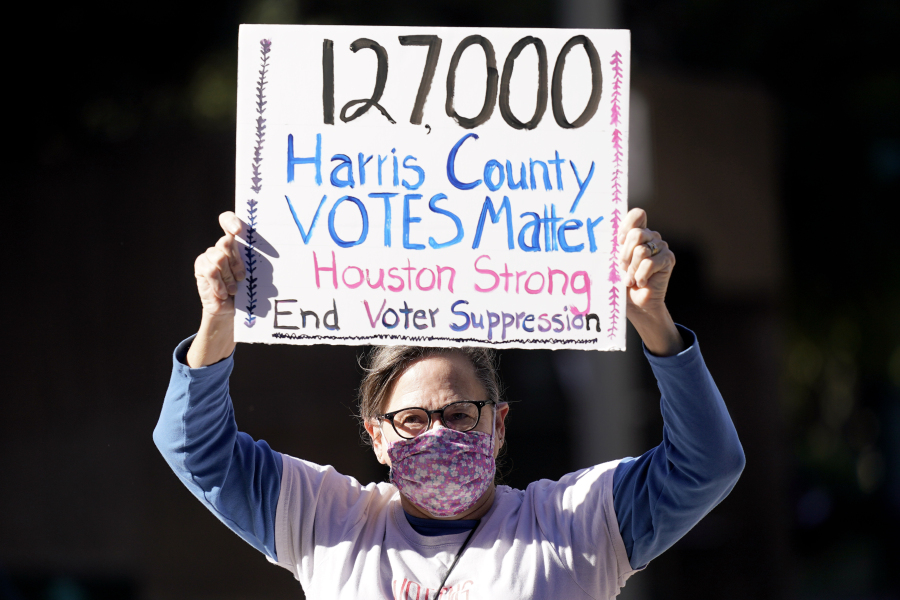 FILE - Demonstrator Gina Dusterhoft holds up a sign as she walks to join others standing across the street from the federal courthouse in Houston, Monday, Nov. 2, 2020, before a hearing in federal court involving drive-thru ballots cast in Harris County. (AP Photo/David J.