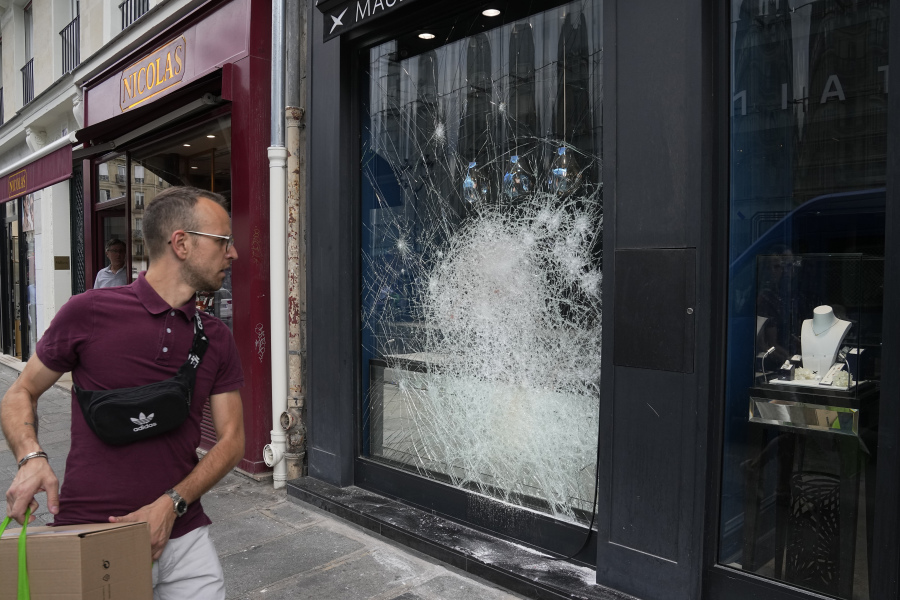 A man walks past a smashed jewelry shop window after a third night of unrest, Friday, June 30, 2023 in Paris. Protesters erected barricades, lit fires and shot fireworks at police who responded with tear gas and water cannons in French streets overnight as tensions grew over the deadly police shooting of a 17-year-old that has shocked the nation.