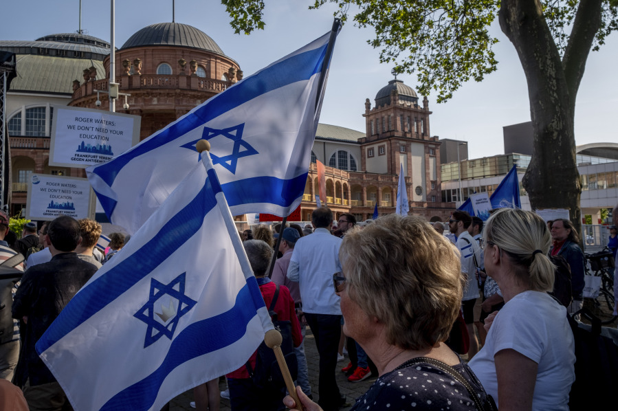 Women hold Israeli flags as they take part in a demonstration against a concert later the day of former Pink Floyd musician Roger Waters in the Festhalle, background, in Frankfurt, Germany, Sunday, May 28, 2023. The Festhalle was the the place where in the night of broken glasses 1938 about 3000 Jewish men where gathered to deport them to concentration camps.