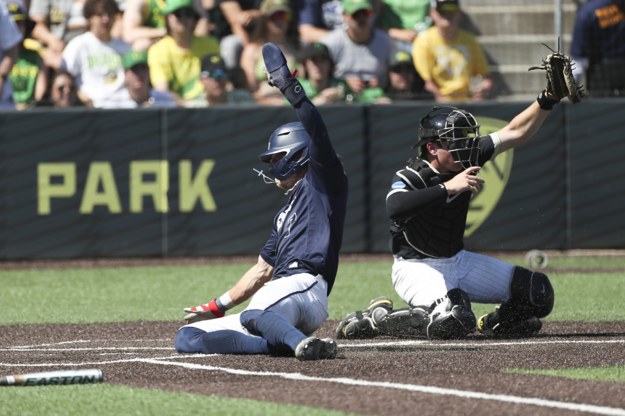Oral Roberts utility Jonah Cox, left, slides home to score past Oregon catcher Bennett Thompson, right, during a NCAA super regional game Sunday in Eugene, Ore.