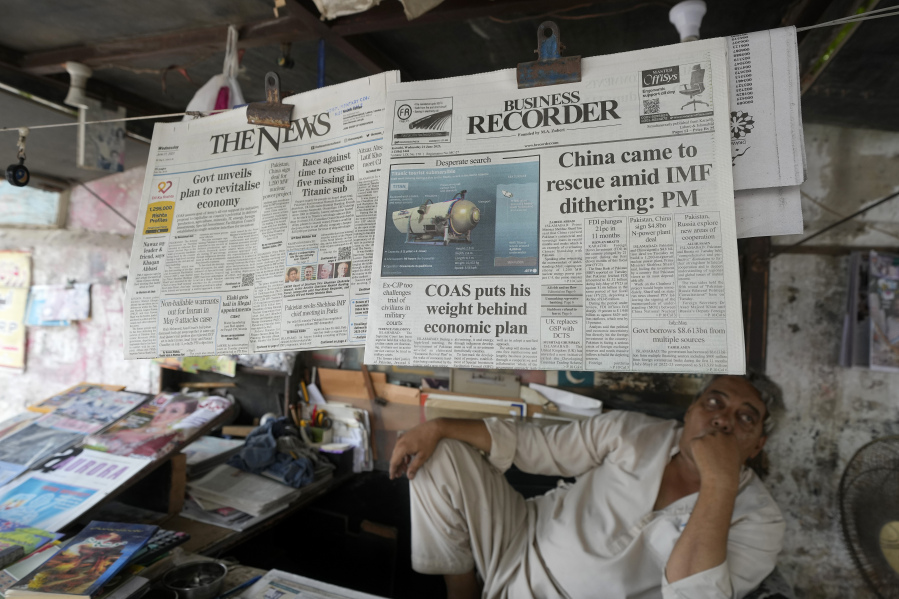 A vendor sits beside a copy of a morning newspaper which reports missing Titanic submersible and onboard five people, including Pakistani nationals Shahzada Dawood and his son Suleman, at a stall, in Karachi, Pakistan, Wednesday, June 21, 2023. A Canadian military surveillance aircraft detected underwater noises as a massive operation searched early Wednesday in a remote part of the North Atlantic for a submersible that vanished while taking five people down including Dawood, a well-known Pakistani businessman and his 19-year-old son to the wreck of the Titanic.