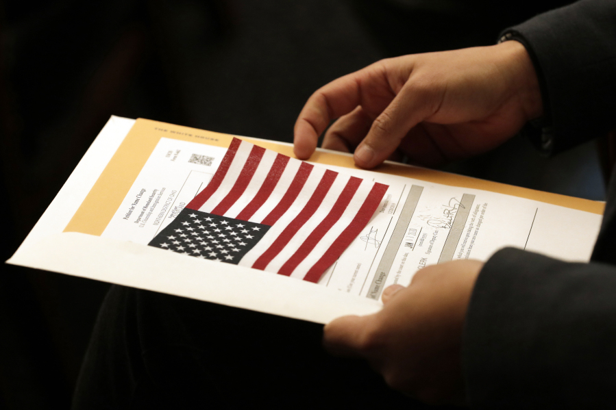 FILE - Abdullah Omar, from Iraq, holds his information packet and an American flag during a naturalization ceremony on Jan. 17, 2020, in Cleveland. Two decades after the U.S. invasion of Iraq, thousands of Iraqis are still trying to emigrate to the United States. An estimated 164,000 Iraqis have already found homes in America since the 2003 invasion. But many are still waiting.