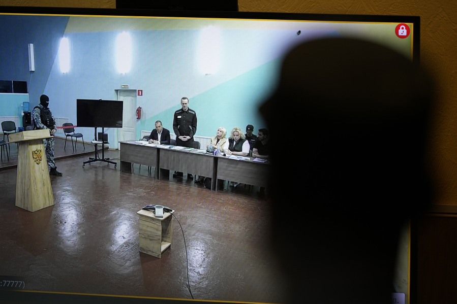 An officer stands in front of a TV screen showing Russian opposition leader Alexei Navalny, standing, speaking between his lawyers in a courtroom, via video link provided by the Russian Federal Penitentiary Service, during a preliminary hearing in the colony, in Melekhovo, Vladimir region, about 260 kilometers (163 miles) northeast of Moscow, Russia, on Monday, June 19, 2023. A Russian court has opened a new trial of imprisoned Russian opposition leader Alexei Navalny that could keep him behind bars for decades.