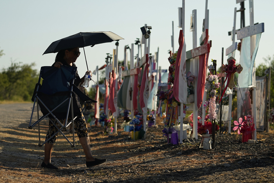 With temperatures hitting triple digits, a woman walks along some of the 53 crosses that are part of a makeshift memorial at the site where officials found dozens of people dead in an abandoned semitrailer containing suspected migrants last summer, Tuesday, June 27, 2023, in San Antonio. U.S. authorities on Tuesday announced the arrests of four more people in connection to the smuggling deaths.