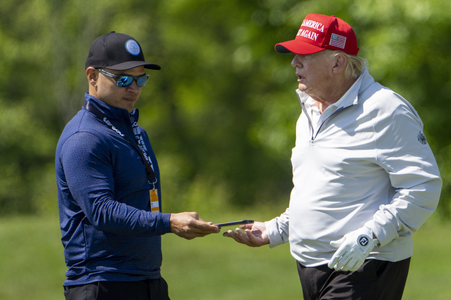 Walt Nauta, left, takes a phone from Former President Donald Trump during the LIV Golf Pro-Am at Trump National Golf Club, Thursday, May 25, 2023, in Sterling, Va. When Trump appears in federal court in Miami, he will likely be joined on the witness stand by a man well-practiced in standing by his side: auta, his valet turned co-conspirator.