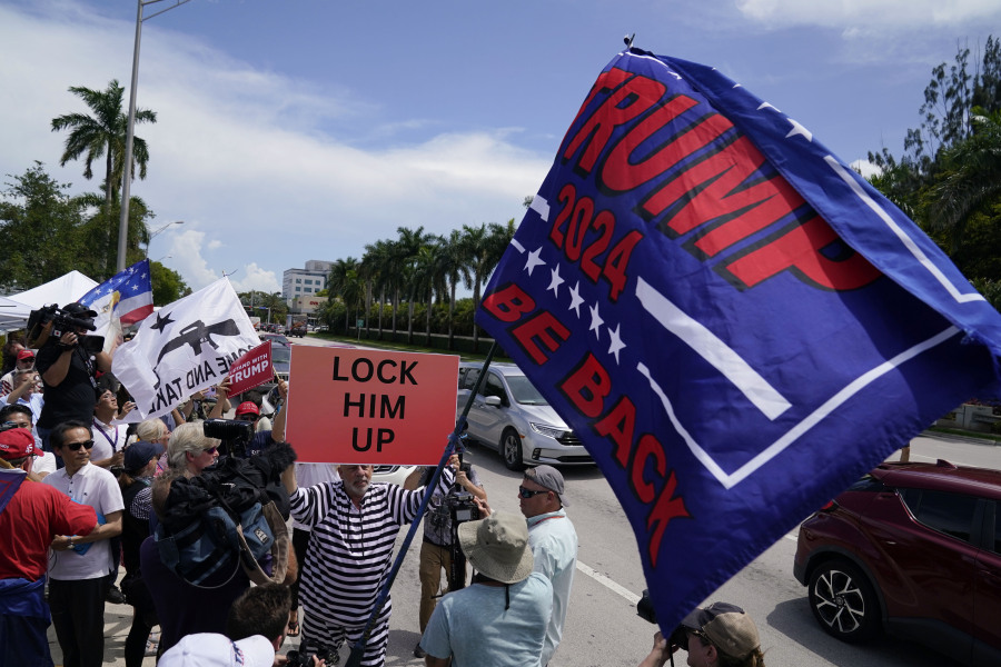 A demonstrator holds a sign that reads "Lock Him Up" as members of the media, protesters and supporters of former President Donald Trump wait for Trump to arrive at Trump National Doral, Monday, June 12, 2023, in Doral, Fla.