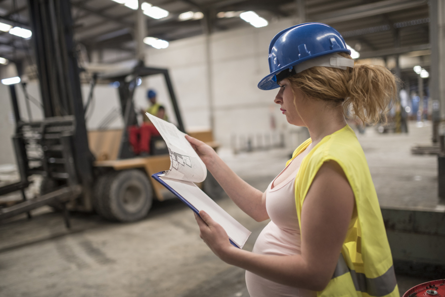 Pregnant woman working and forklift in bakcground
