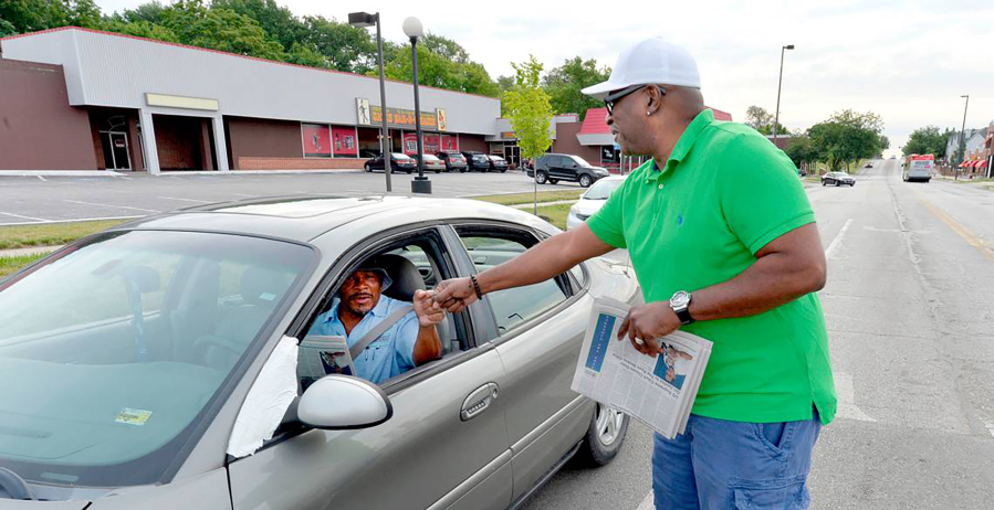 Eric Wesson, publisher of the new weekly newspaper The Next Page KC, fist bumps a driver while handing out free copies of his paper at 12th Street and Brooklyn Avenue.