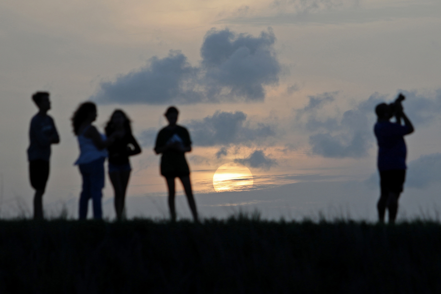 People watch as the sun sets behind clouds on Sunday, May 22, 2022, in Coral Springs. A patch of Saharan dust arrived late Friday and overnight Saturday, which may cause hazy conditions and hue-altered sunrises and sunsets.