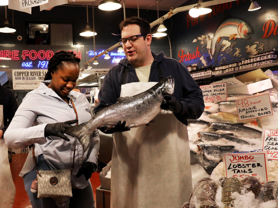 Joydie Ellis, visiting Seattle's Pike Place Market, wanted to have a souvenir photograph at the Pure Food Fish Market's stand and co-owner Isaac Behar suggested adding a king salmon to the image.