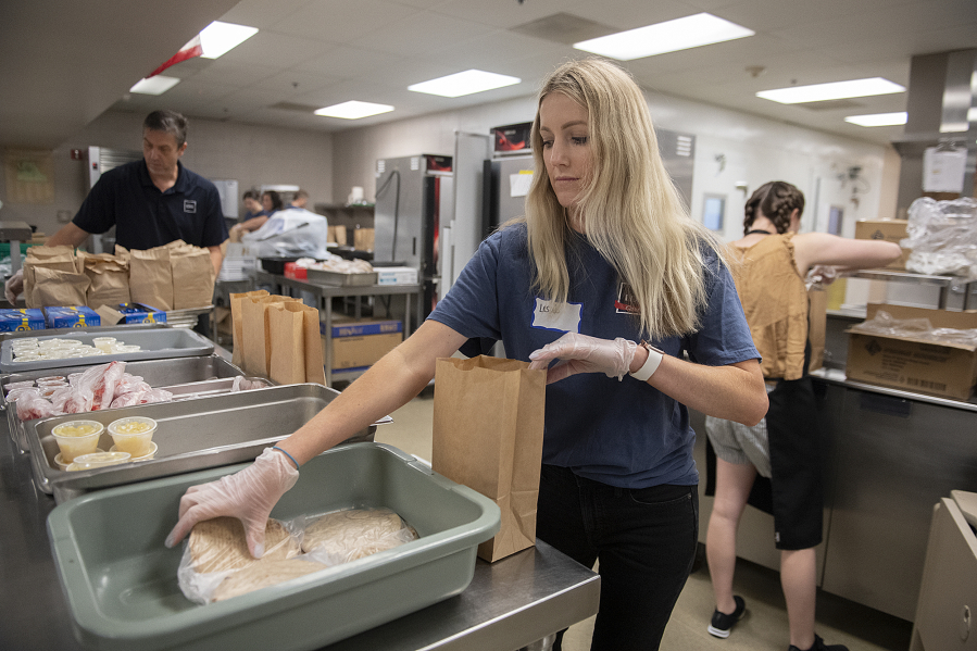 Volunteers Leslie Matheney, center, and Vitaliy Shkurov, left, of IDM Cos. help assemble lunches for kids in need while working in the kitchen at Fort Vancouver High School. Share is celebrating the 20th anniversary of its summer meal program.