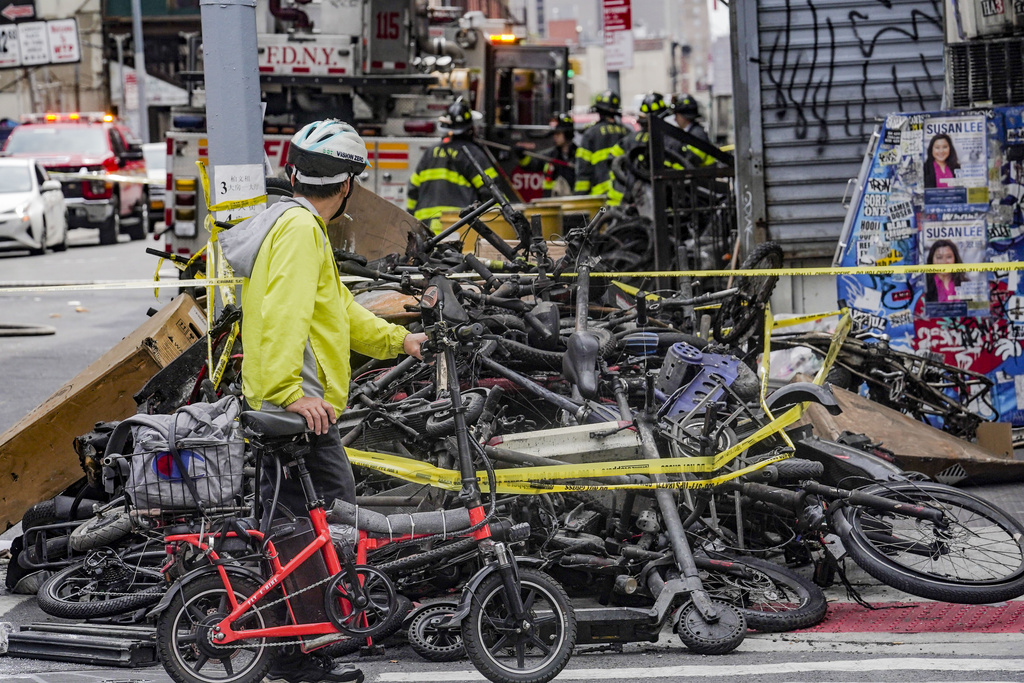 FILE - A biker stops to look at a pile of e-bikes in the aftermath of a fire in Chinatown, which authorities say started at an e-bike shop and spread to upper-floor apartments, Tuesday June 20, 2023, in New York. Federal officials are looking into cracking down on defective lithium-ion batteries that power hoverboards, scooters and motorized bicycles because of a rash of deadly fires caused by exploding batteries. The effort comes as New York City implements new laws meant to reduce the number of fires, injuries and deaths in a city where e-bikes have become ubiquitous.