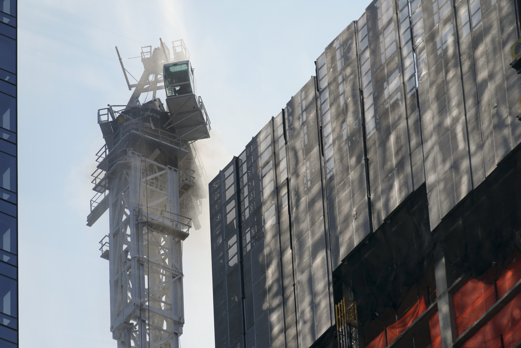 Smoke rises from a construction crane that caught fire in Manhattan, Wednesday, July 26, 2023, in New York.  The crane lost its long arm, which smashed against a nearby building, dangled and then plummeted to the street as people ran for their lives on the sidewalk below.
