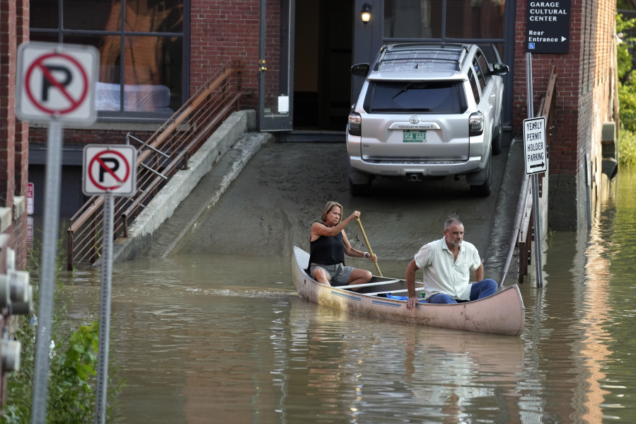 Jodi Kelly, left, practice manager at Stonecliff Veterinary Surgical Center, behind, and her husband, veterinarian Dan Kelly, use a canoe to remove surgical supplies from the flood-damaged center, Tuesday, July 11, 2023, in Montpelier, Vt. The supplies included orthopedic implants for an upcoming surgery on a dog. A storm that dumped two months of rain in two days brought more flooding across Vermont Tuesday.