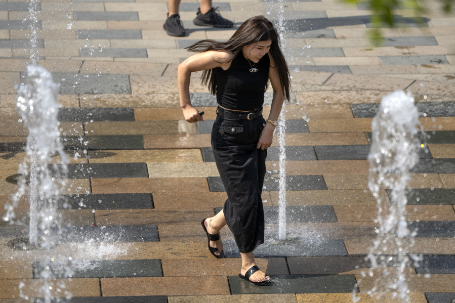 A woman runs through a fountain at a shopping mall in Beijing, Friday, June 23, 2023. Authorities issued a rare red alert for high temperatures in parts of China's capital on Friday, the highest level of warning, as highs were expected to once again climb to around 40 degrees Celsius (104 degrees Farenheit).