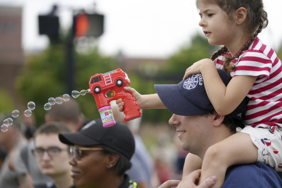 Madeline Couper, four years old, blows bubbles on the Fourth of July parade while sitting on her father, firefighter Jon Cooper's shoulders, Tuesday, July 4, 2023, in Pittsfield, Ma..
