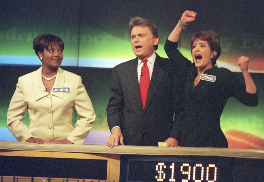 FILE - Johnna Goodwin, left, watches as Donna Handel, right, reacts after winning on "Wheel of Fortune," with host Pat Sajak during a taping of the game show in Philadelphia on April 17, 1999. The game show was in Philadelphia for the weekend taping a week's worth of shows.